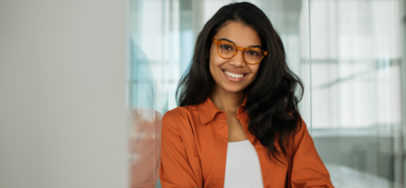 Woman with glasses and orange shirt smiling with arms folded