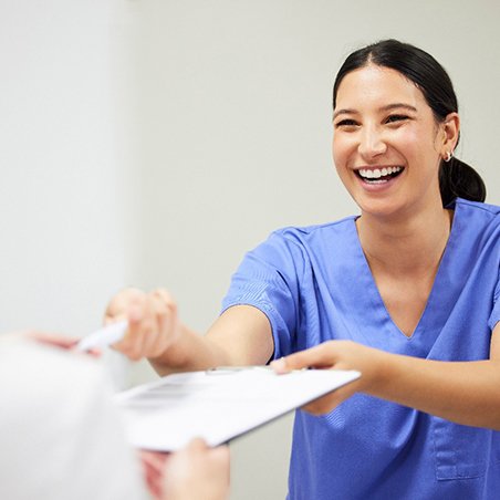 Woman in blue scrubs handing forms and pen to patient