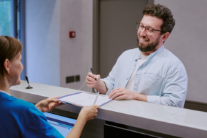 a smiling man wearing glasses signing up for a dental membership plan at his dental office