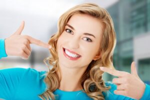 Woman smiling and pointing to her white, straight teeth. 